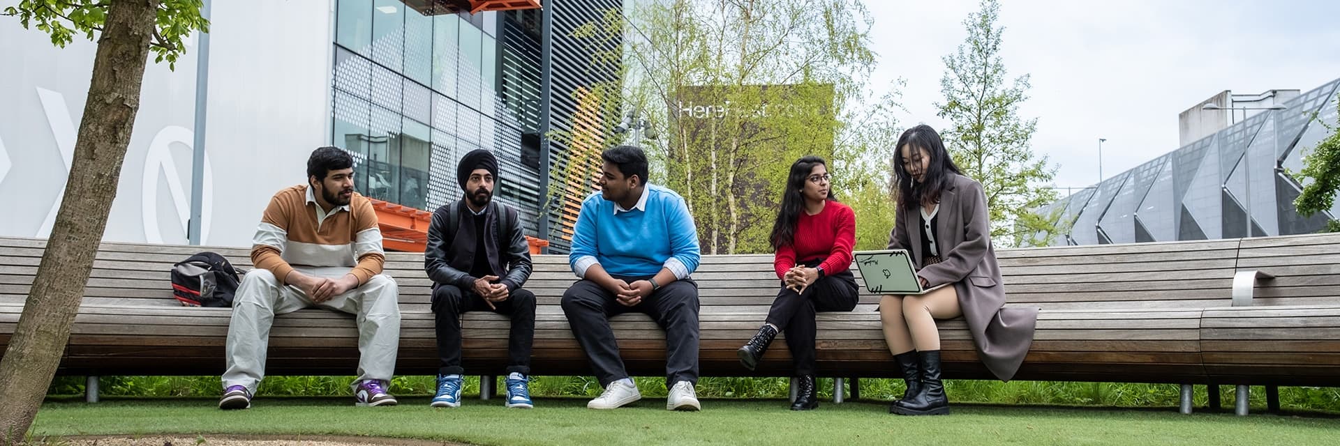 Five students sitting on a bench outside on the Loughborough University London campus